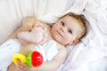 Cute little baby playing with toy rattle and own feet after taking bath. Adorable beautiful girl wrapped in white towels Royalty Free Stock Photo