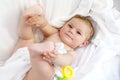 Cute little baby playing with toy rattle and own feet after taking bath. Adorable beautiful girl wrapped in white towels Royalty Free Stock Photo