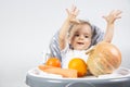 A cute little baby sits on a high chair and in front of him carrots, pumpkin and oranges on a white background. Vitamins for Royalty Free Stock Photo