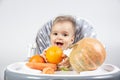 A cute little baby sits on a high chair and in front of him carrots, pumpkin and oranges on a white background. Vitamins for Royalty Free Stock Photo