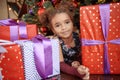 Beautiful kid girl 5-6 year old wearing stylish dress sitting in armchair over Christmas tree in room. Looking at camera. Holiday