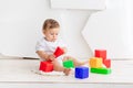 Cute little baby six months old in a white t shirt and diapers playing at home on a Mat in a bright room with bright colored cubes