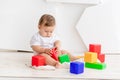 Cute little baby six months old in a white t shirt and diapers playing at home on a Mat in a bright room with bright colored cubes