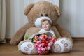 Cute little baby smiling with his first teeth, sitting on huge teddy bear with big bouquet of tulips Royalty Free Stock Photo