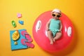 Cute little baby in sunglasses with inflatable ring and beach accessories on yellow background, top view Royalty Free Stock Photo