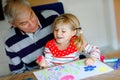 Cute little baby toddler girl and handsome senior grandfather painting with colorful felt pens and pencils at home Royalty Free Stock Photo