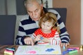 Cute little baby toddler girl and handsome senior grandfather painting with colorful felt pens and pencils at home Royalty Free Stock Photo