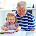 Cute little baby toddler girl and handsome senior grandfather painting with colorful pencils at home. Grandchild and man Royalty Free Stock Photo