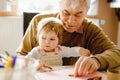 Cute little baby toddler girl and handsome senior grandfather painting with colorful pencils at home. Grandchild and man having Royalty Free Stock Photo