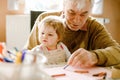 Cute little baby toddler girl and handsome senior grandfather painting with colorful pencils at home. Grandchild and man Royalty Free Stock Photo