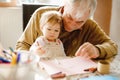 Cute little baby toddler girl and handsome senior grandfather painting with colorful pencils at home. Grandchild and man Royalty Free Stock Photo