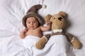 Cute little baby with toy bear lying under blanket in bed Royalty Free Stock Photo