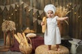 Cute little baby wearing baker costume with a French baguette in a rustic interior Royalty Free Stock Photo