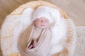Cute little baby in white knitted hat lies in a wicker basket in a beige knitted blanket. Summer mood. Royalty Free Stock Photo