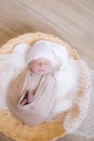 Cute little baby in white knitted hat lies in a wicker basket in a beige knitted blanket. Summer mood. Royalty Free Stock Photo