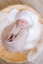 Cute little baby in white knitted hat lies in a wicker basket in a beige knitted blanket. Summer mood. Royalty Free Stock Photo