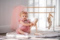 A cute little ballerina in a pink ballet costume sits near the barre in the room and tries to put on her pointe shoes. Kid and Royalty Free Stock Photo