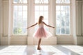 Cute little ballerina wearing pink dress dancing in white sunny studio. Girl in dance class. Child practicing ballet