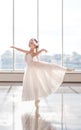 Cute little ballerina in white ballet costume and pointe shoes with is dancing in the room