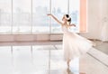 Cute little ballerina in white ballet costume and pointe shoes is dancing in the room