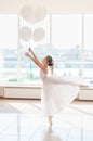 Cute little ballerina in white dress and pointe shoes with white balloons is dancing in the room Royalty Free Stock Photo