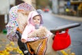 Cute little beautiful baby girl sitting in the pram or stroller on autumn day. Happy smiling child in warm clothes Royalty Free Stock Photo