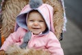 Cute little beautiful baby girl sitting in the pram or stroller on autumn day. Happy smiling child in warm clothes Royalty Free Stock Photo