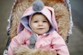 Cute little beautiful baby girl sitting in the pram or stroller on autumn day. Happy smiling child in warm clothes Royalty Free Stock Photo