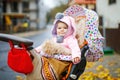 Cute little beautiful baby girl sitting in the pram or stroller on autumn day. Happy smiling child in warm clothes Royalty Free Stock Photo
