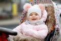 Cute little beautiful baby girl sitting in the pram or stroller on cold autumn, winter or spring day. Happy smiling Royalty Free Stock Photo