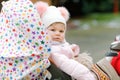 Cute little beautiful baby girl sitting in the pram or stroller on cold autumn, winter or spring day. Happy smiling Royalty Free Stock Photo