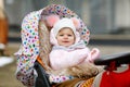 Cute little beautiful baby girl sitting in the pram or stroller on cold autumn, winter or spring day. Happy smiling Royalty Free Stock Photo