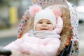 Cute little beautiful baby girl sitting in the pram or stroller on cold autumn, winter or spring day. Happy smiling Royalty Free Stock Photo