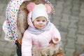 Cute little beautiful baby girl sitting in the pram or stroller on cold autumn, winter or spring day. Happy smiling Royalty Free Stock Photo