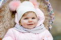 Cute little beautiful baby girl sitting in the pram or stroller on cold autumn, winter or spring day. Happy smiling Royalty Free Stock Photo