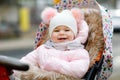 Cute little beautiful baby girl sitting in the pram or stroller on cold autumn, winter or spring day. Happy smiling Royalty Free Stock Photo