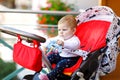 Cute little beautiful baby girl sitting in the pram or stroller and waiting for mom. Happy smiling child with blue eyes Royalty Free Stock Photo