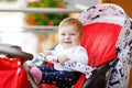 Cute little beautiful baby girl sitting in the pram or stroller and waiting for mom. Happy smiling child with blue eyes. Royalty Free Stock Photo