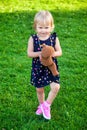 Cute little blond baby girl two year old playing with teddy bear on fresh green grass with flowers Royalty Free Stock Photo