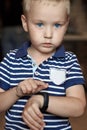 Cute little blond boy with blue eyes points out to digital fitness tracker on his wrist. Serious expression, strong emotions, chil