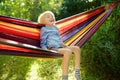 Cute little blond caucasian boy having fun with multicolored hammock in backyard or outdoor playground. Summer active leisure for Royalty Free Stock Photo