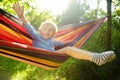 Cute little blond caucasian boy having fun with multicolored hammock in backyard or outdoor playground. Summer active leisure for Royalty Free Stock Photo