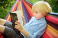 Cute little blond caucasian boy reading book and having fun with multicolored hammock in backyard or outdoor playground. Summer Royalty Free Stock Photo