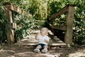 Cute Little Blond Haired Toddler Boy Kid Child Sitting and Laughing in Front of Wooden Bridge Over a Creek at the Outdoor Park in Royalty Free Stock Photo