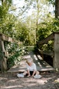 Cute Little Blond Haired Toddler Boy Kid Child Sitting and Laughing in Front of Wooden Bridge Over a Creek at the Outdoor Park in Royalty Free Stock Photo