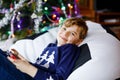 Cute little blond kid boy playing with a video game on gadget console on Christmas with decorated tree on background Royalty Free Stock Photo