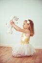 Cute little blonde ballerina in tutu holding white teddy bear toy in hands