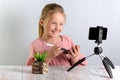 Cute little blonde beauty blogger. Girl speaking in front of the camera for Vlog. A beautiful smiling schoolgirl sits at a table Royalty Free Stock Photo