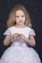 Cute little blonde girl in a beautiful white dress on a dark background Royalty Free Stock Photo