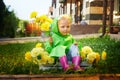 Cute little blonde girl in green raincoat sitting in a box with yellow flowers on a green lawn under rain drops or the Royalty Free Stock Photo